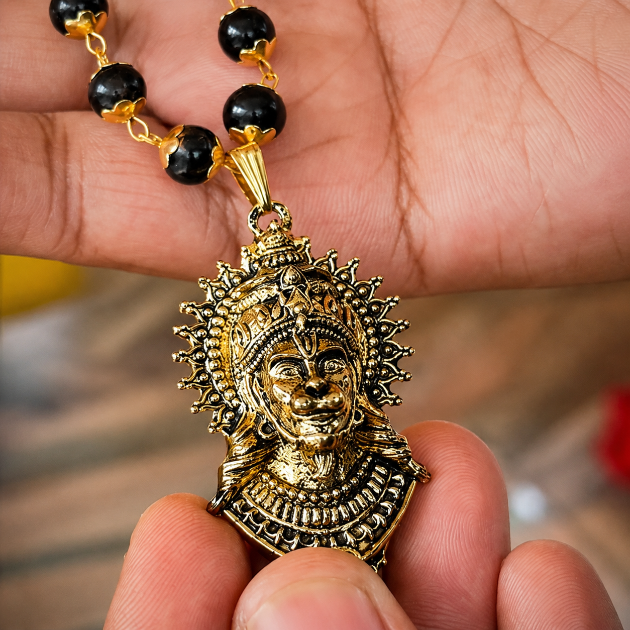 Gold and black beaded necklace with a detailed pendant held in a hand.