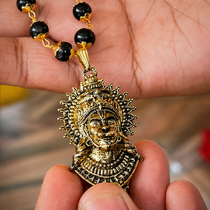 Gold and black beaded necklace with a detailed pendant held in a hand.