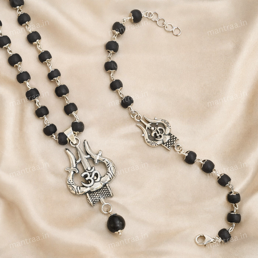 Om Trishul Karungali Bracelet & Necklace Combo - Silver Plated Black beaded necklace with silver pendants on a beige fabric background